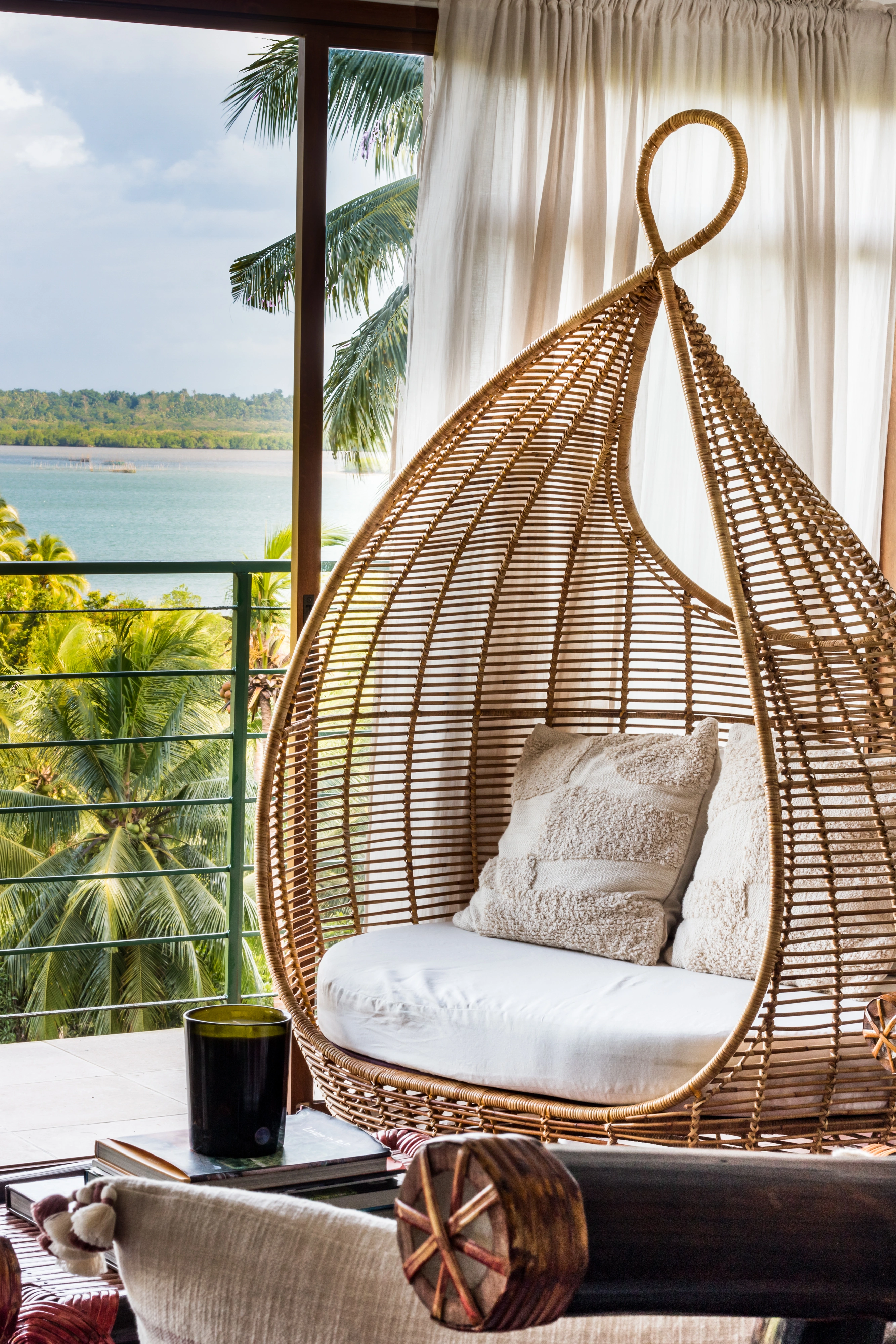 Fauteuil suspendu en rotin à Villa Kulintang, face à la mer et aux palmiers.